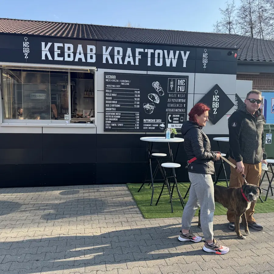 Wysokie stoliki przed czarnym pawilonem Kebbz